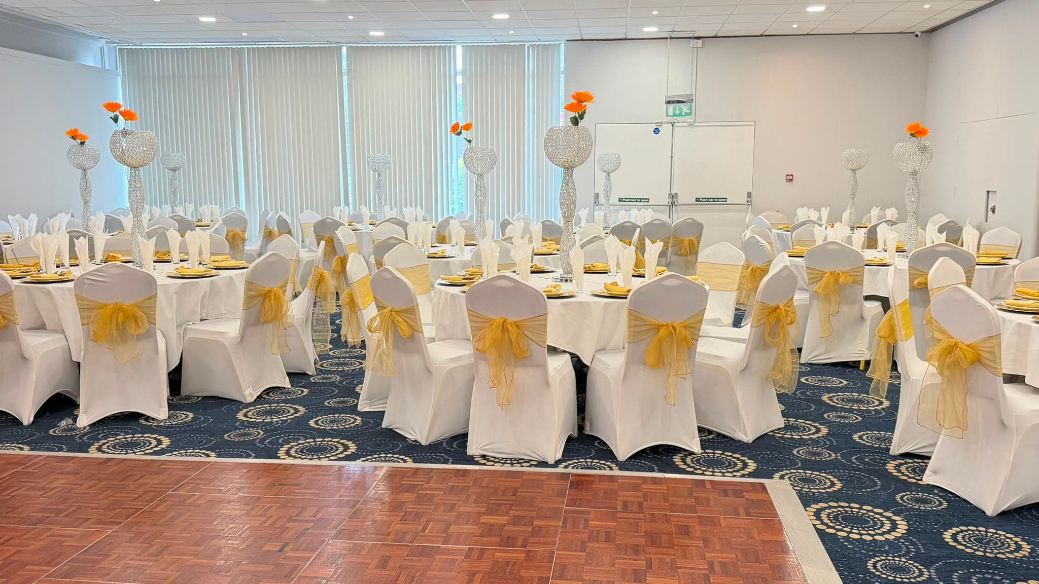 Rows of white chair covers tied with gold organza sashes, crystal candelabra centrepieces topped with orange gerberas.