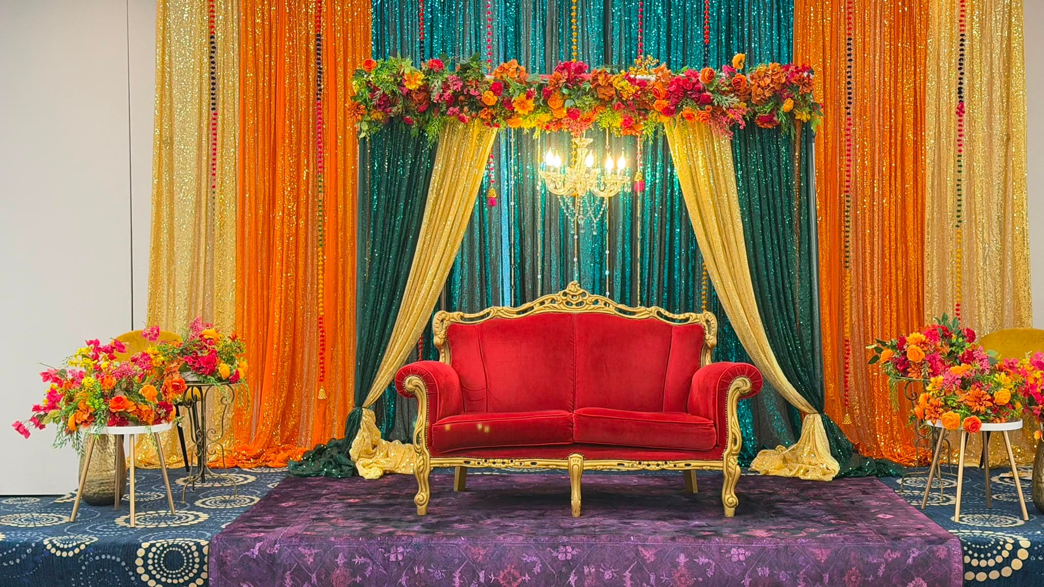 The full wedding stage set on a purple platform, flanked by tall arrangements of marigold and magenta flowers.