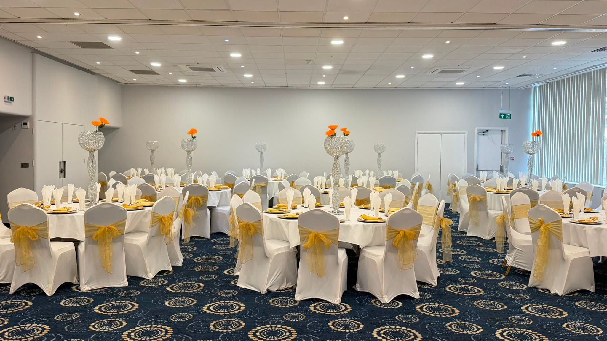 Round tables set for a daytime function, crystal centrepieces with marigold flowers throughout.